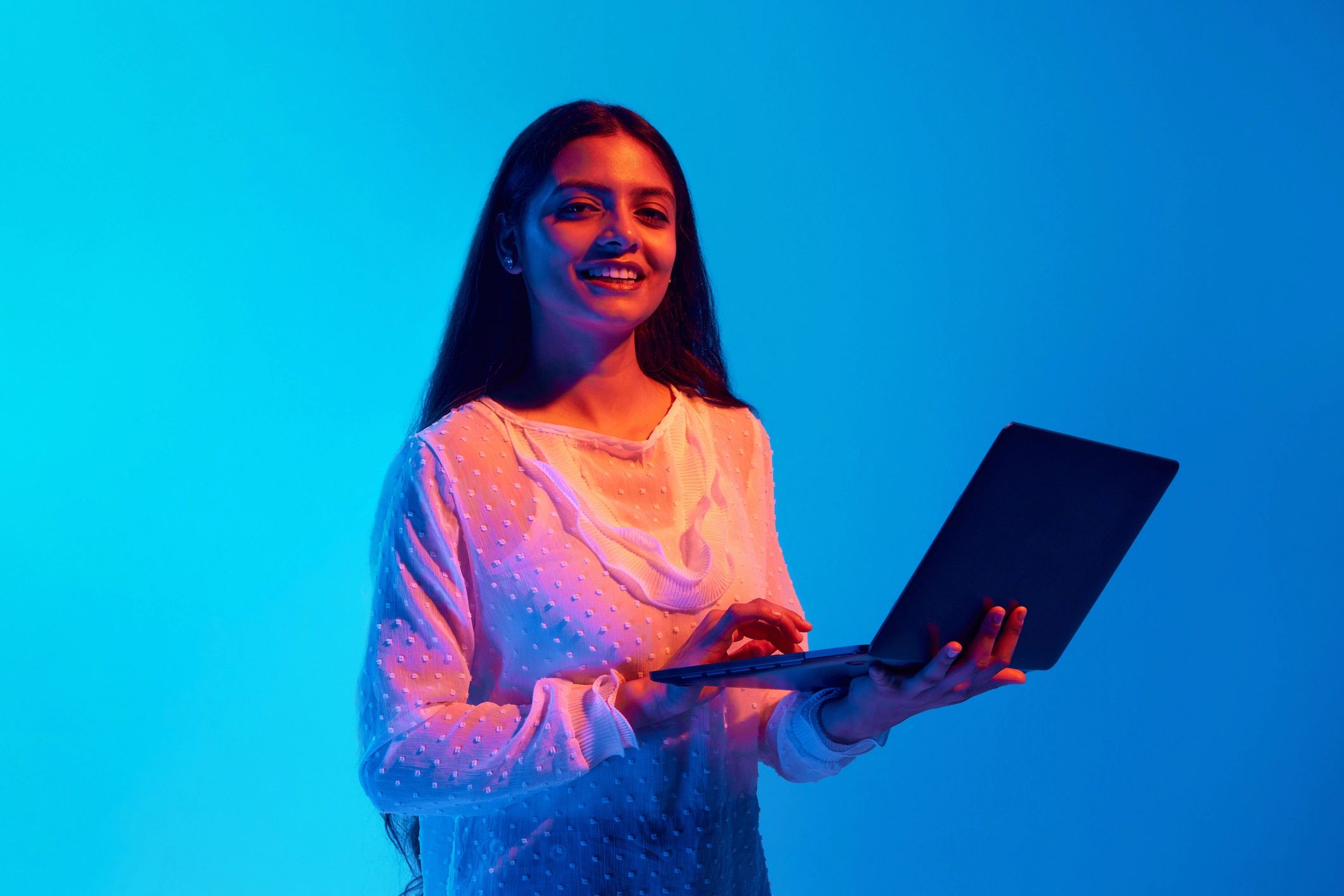 Woman entrepreneur holding a laptop in a bright blue setting